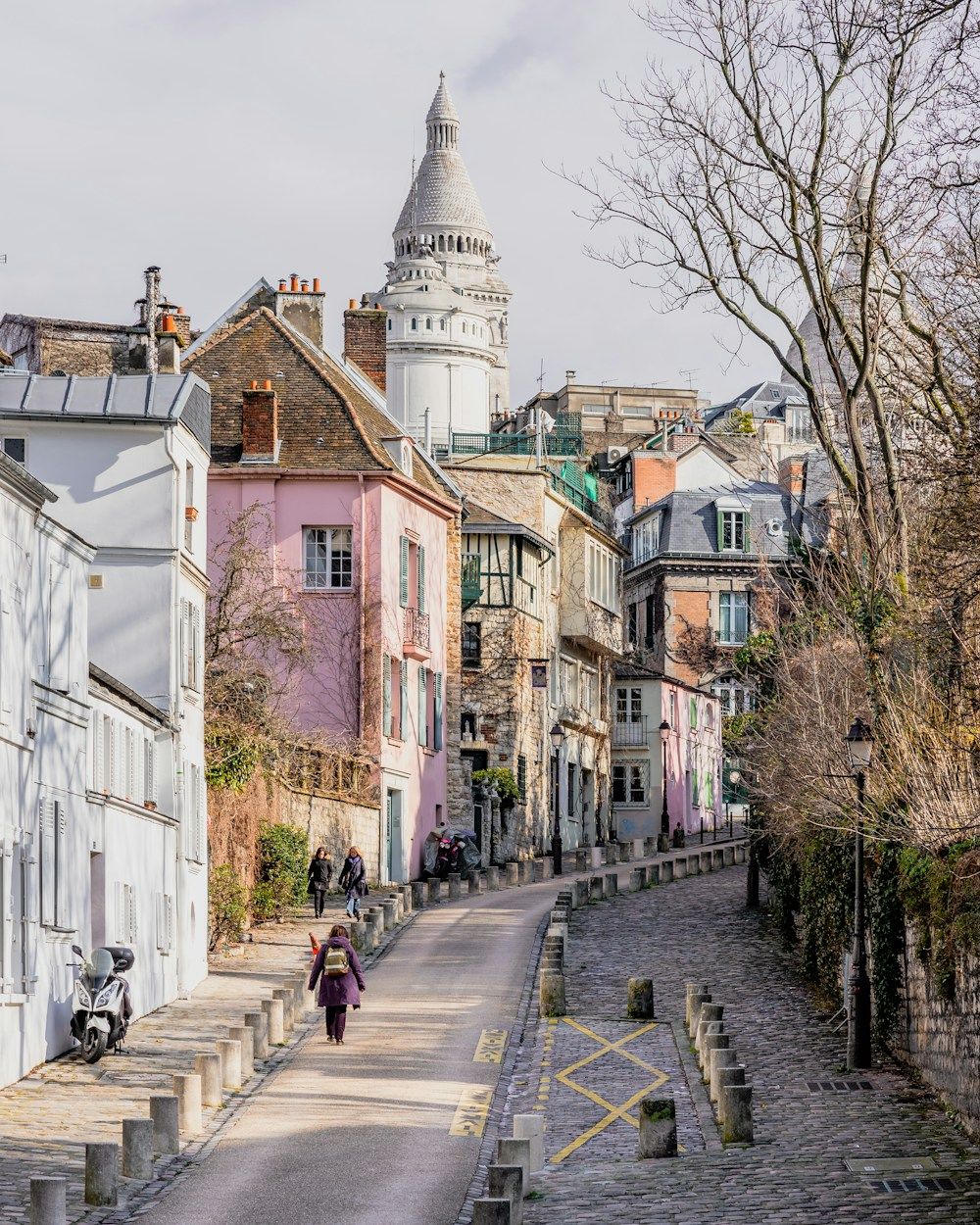 The winding Rue de l’Abreuvoir, lined with facades and cobblestones, with the Sacré-Cœur dome above.