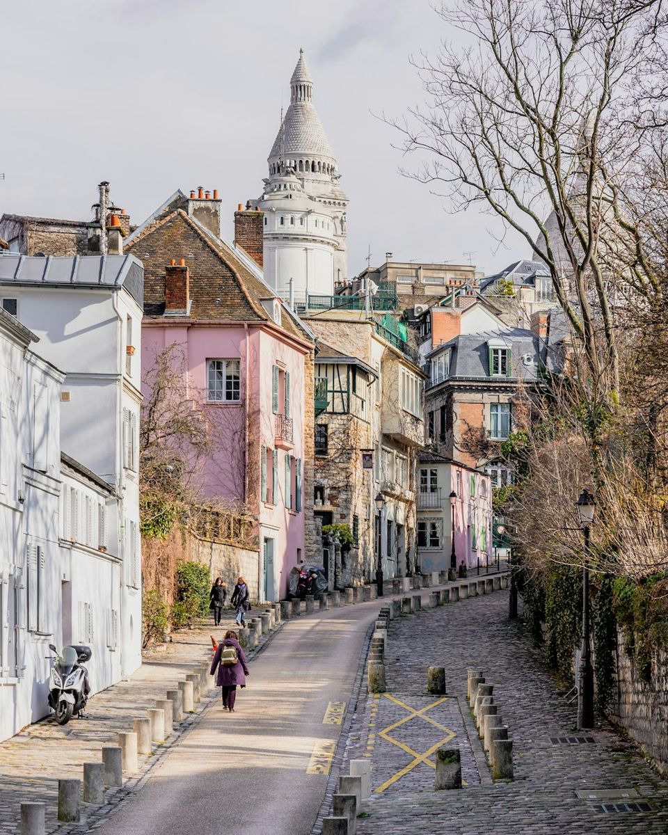 The winding Rue de l’Abreuvoir, lined with facades and cobblestones, with the Sacré-Cœur dome above.