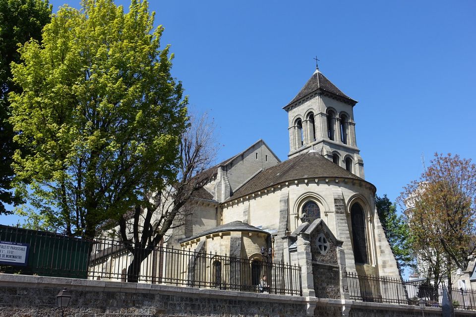 The stone apse and bell tower of Saint-Pierre de Montmartre beneath a blue sky.
