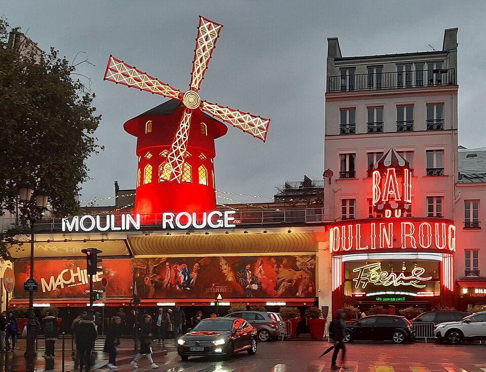The Moulin Rouge at dusk, its red windmill and illuminated signs above the Boulevard de Clichy