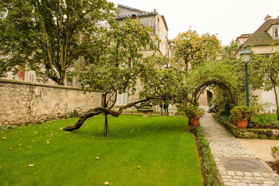 A lawn, leaning tree and cobbled path beneath a leafy arch in the Musée de Montmartre garden, photographed in 2012.