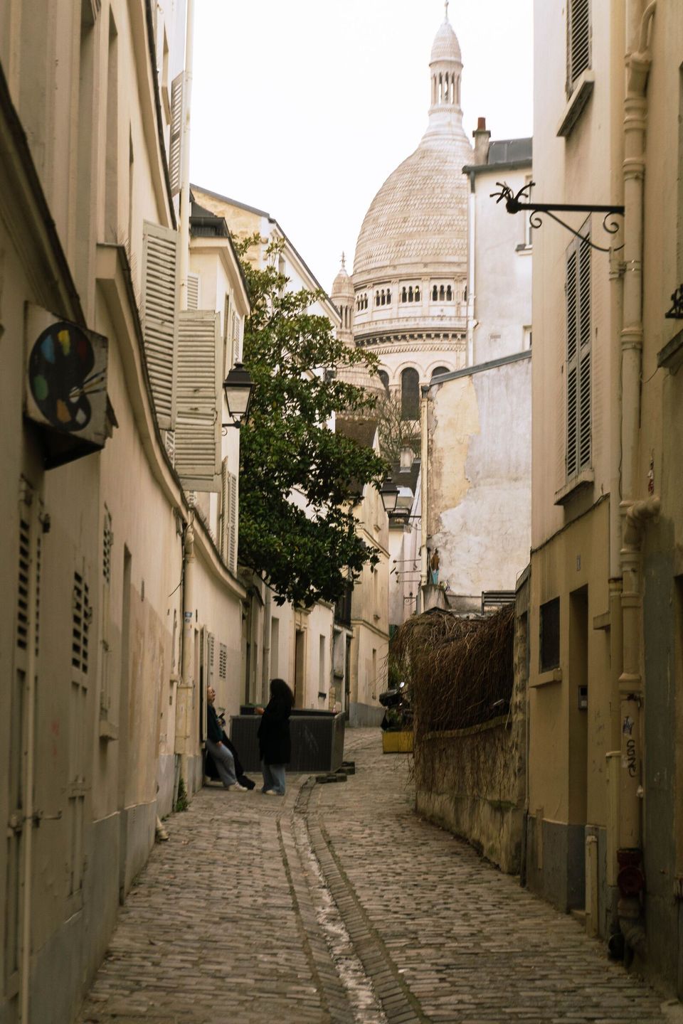 A cobbled Montmartre lane leading toward the dome of the Sacré-Cœur basilica.