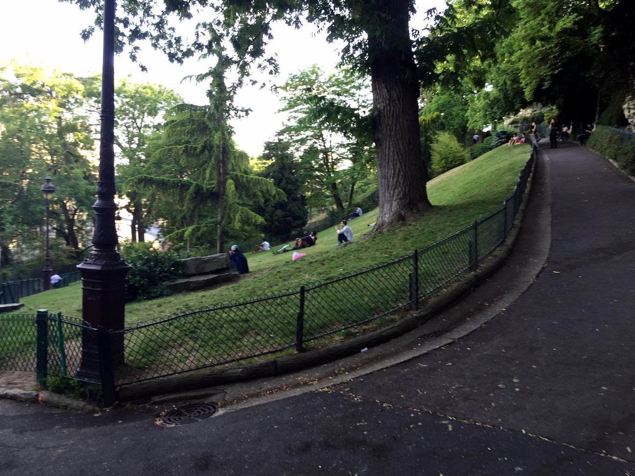 A curving path and grassy slope beneath trees in Square Louise-Michel, photographed in June 2015.